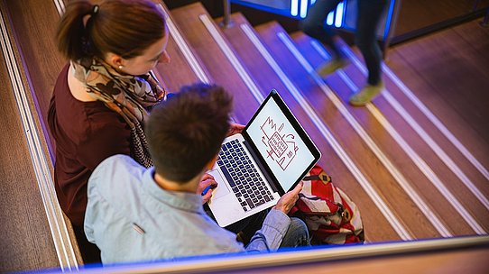 Auf der Treppe sitzend, planen zwei Studenten ihr IT-Projekt.  