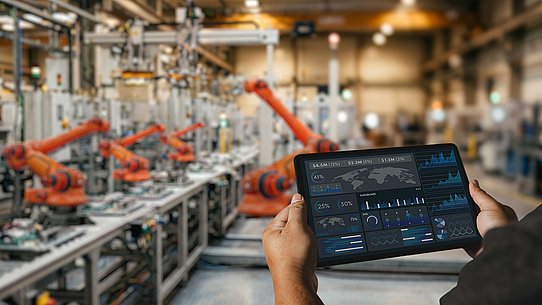 Mann mit iPad steht in Halle mit Robotern. 