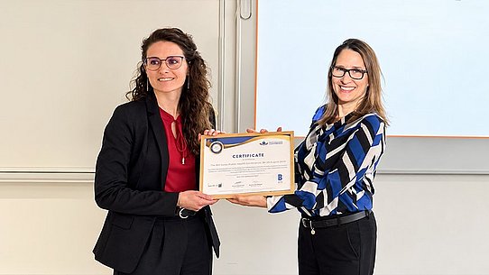 Zwei Frauen halten ein Diplom in der Hand. 