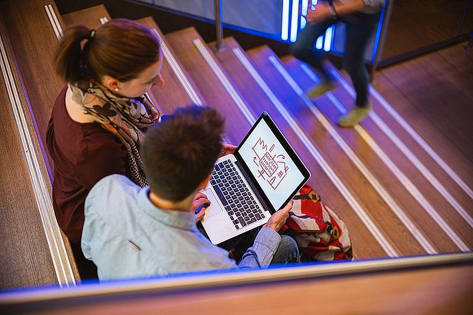 Auf der Treppe sitzend, planen zwei Studenten ihr IT-Projekt.  