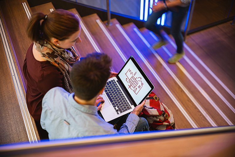 Auf der Treppe sitzend, planen zwei Studenten ihr IT-Projekt.  