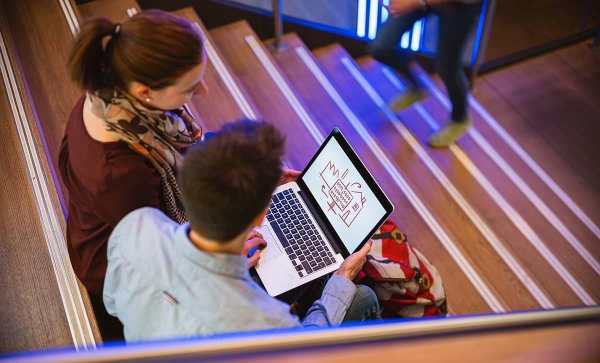 Auf der Treppe sitzend, planen zwei Studenten ihr IT-Projekt.  